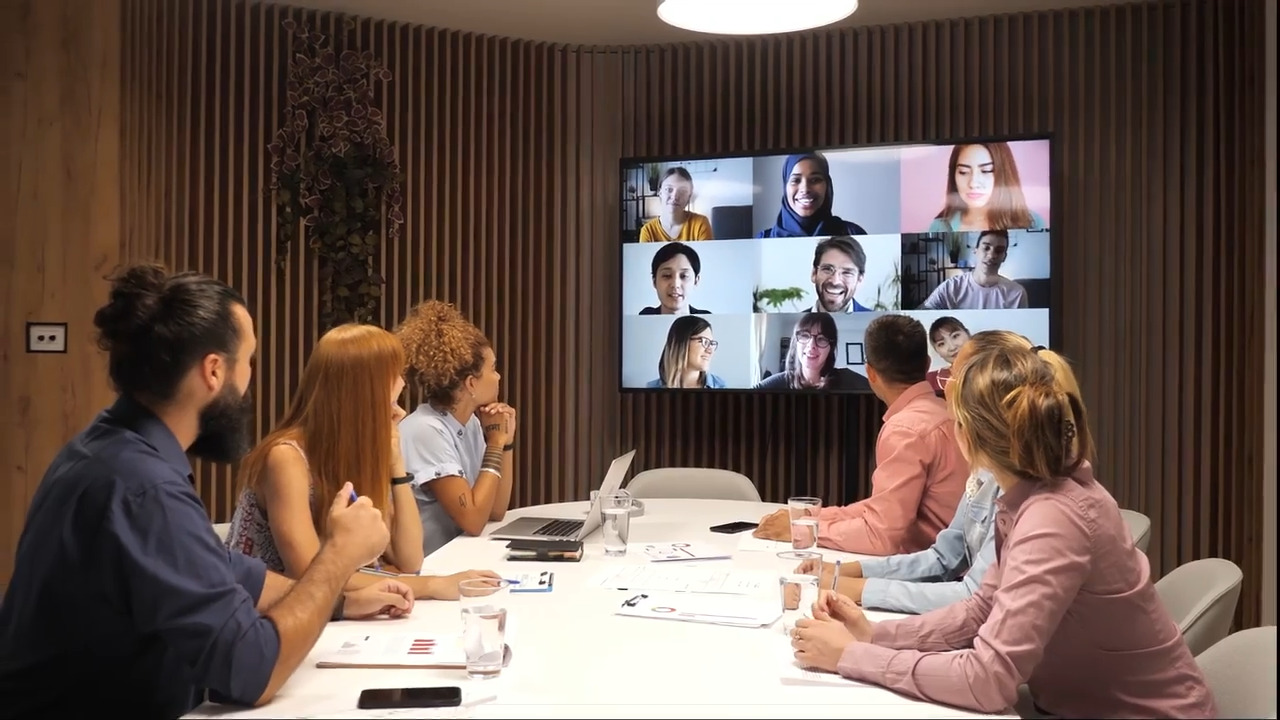 Employees sit at a boardroom table and teleconference with other colleagues