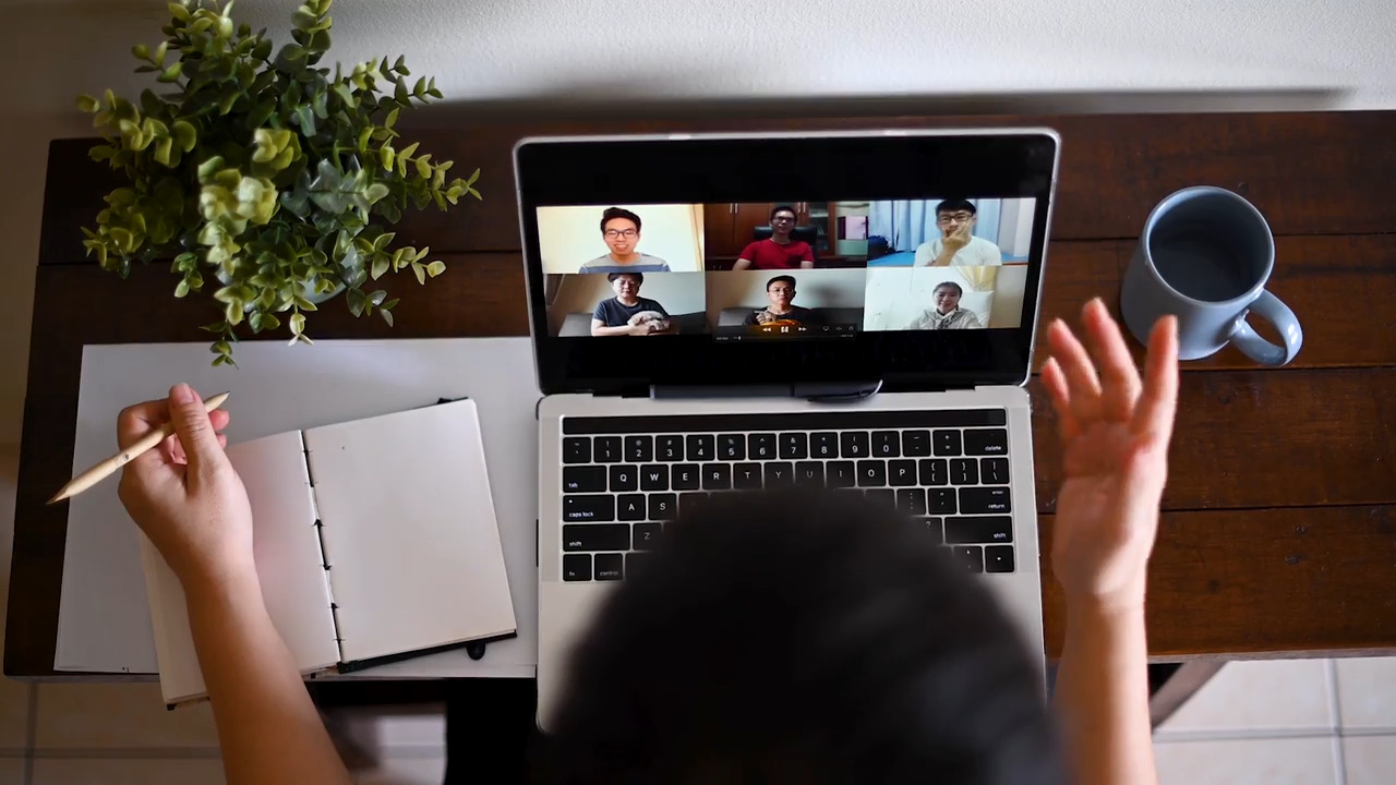 Una persona sentada en un escritorio hablando con otras personas en una videoconferencia. 