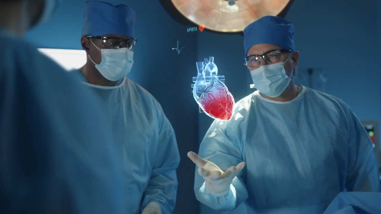 Three doctors standing in a surgical room with two looking at a 3-D rendering of a human heart