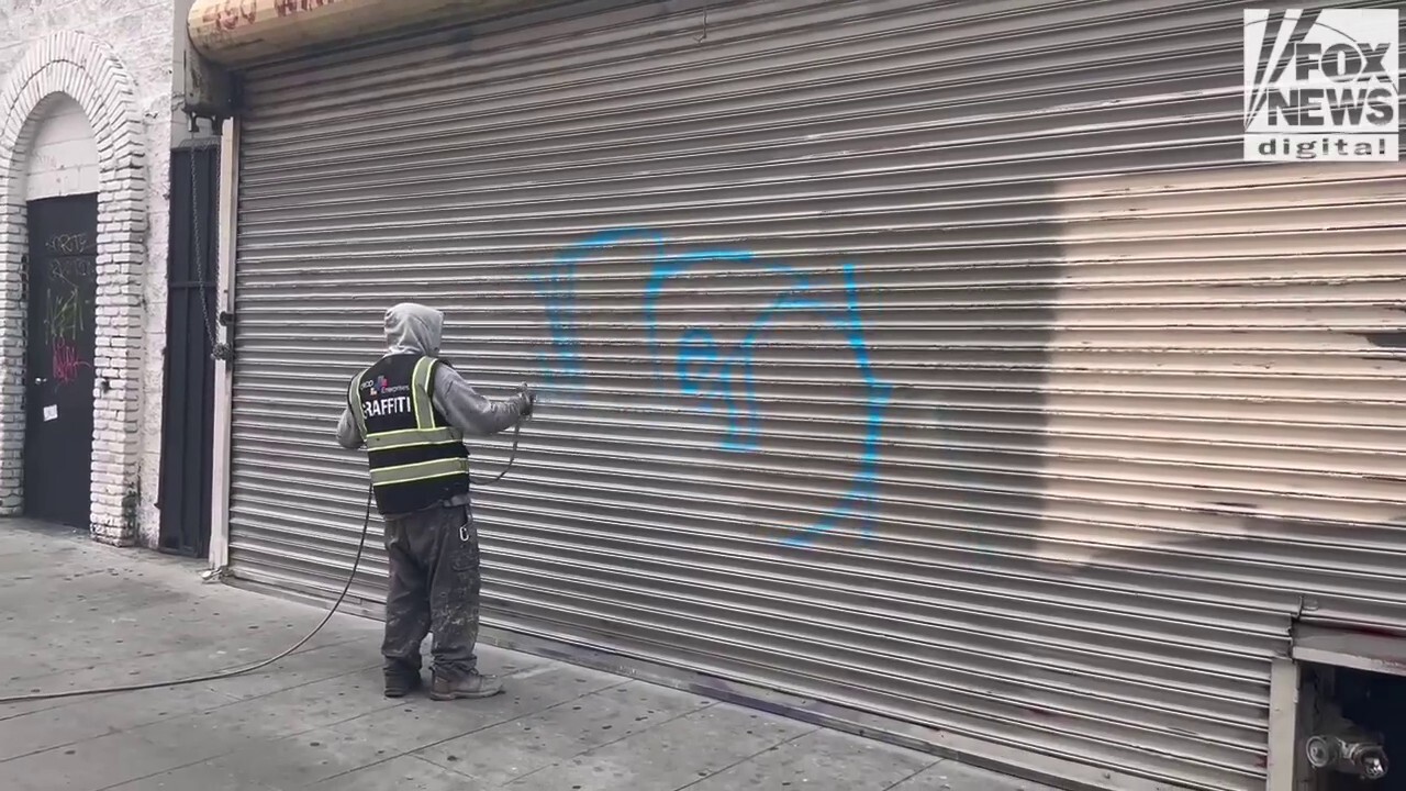 Man paints over graffiti on vandalized garage door in downtown Los Angeles