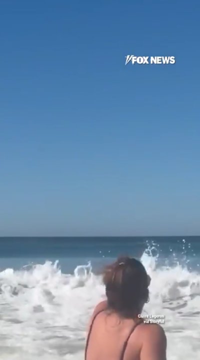 Shark leaps from ocean behind women filming on California beach