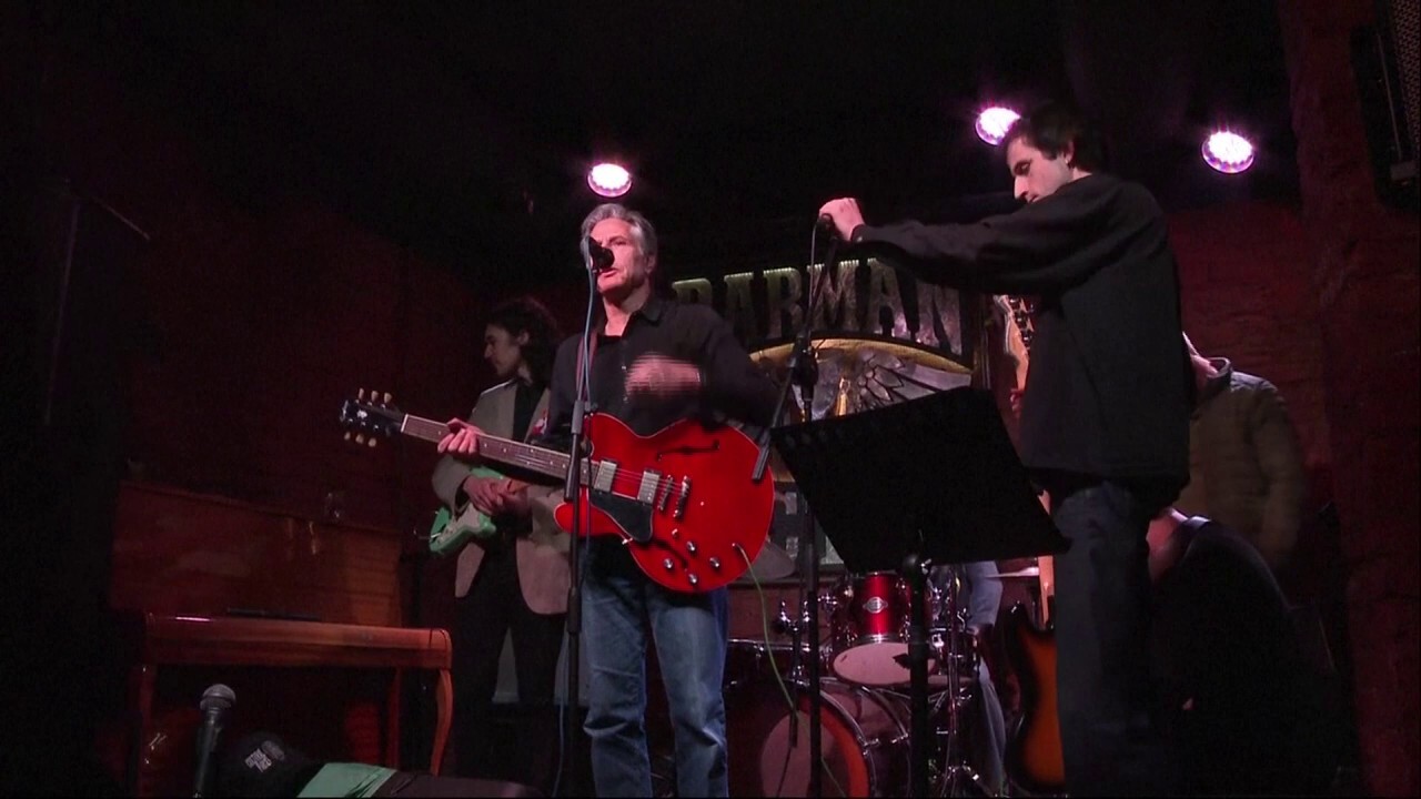 Блинкен, с китара в ръка, пее „Rockin’ in the Free World“ в бар в Киев по време на пътуване до Украйна