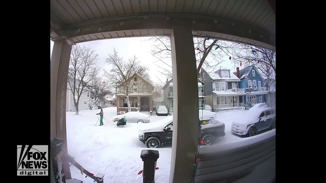 Skier tows child through snowy neighborhood street