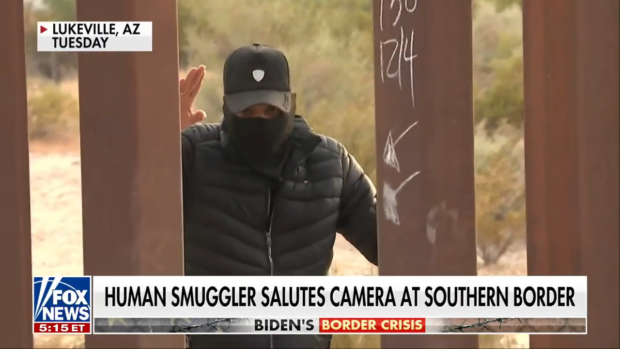 Контрабандист поздравява камерата, докато води мигранти през счупената част от граничната стена